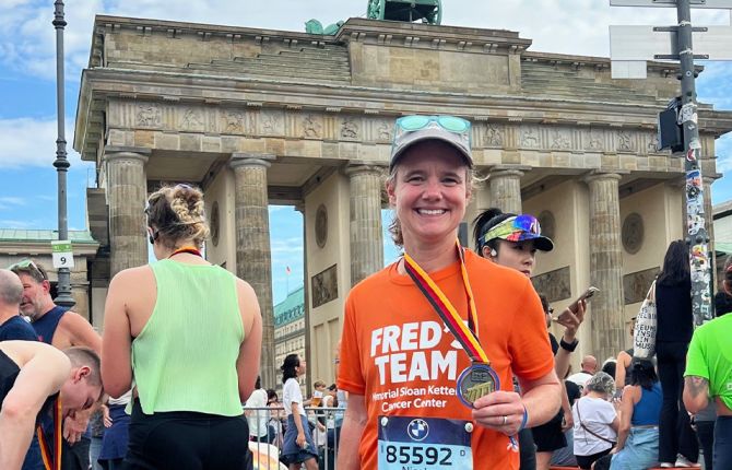 Fred’s Team charity runner Nicole standing in front of the Brandenburg Gate smiling and holding her finisher’s medal from the 2025 BMW Berlin Marathon.