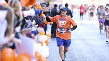 John Fiore has a big smile on his face and one arm outstretched in a high five while running a race. 