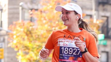 Katie DiBella McIlraith makes the peace sign with a raised hand while running the TCS New York City Marathon. 