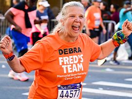 A Fred's Team charity runner wearing an orange uniform participating in the TCS New York City Marathon to raise money for cancer research.