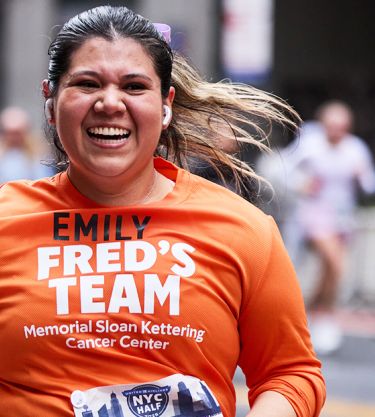 Runner smiling in orange shirt during a marathon, surrounded by other runners.