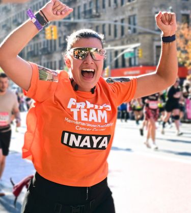 A runner in an orange Fred’s Team tank top smiles as she greets supporters on the sidelines during a race. 