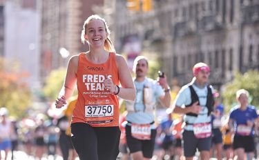 A Fred’s Team participant runs the TCS New York City Marathon in their orange Fred’s Team shirt.