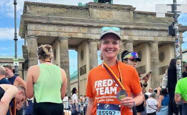 Fred’s Team charity runner Nicole standing in front of the Brandenburg Gate smiling and holding her finisher’s medal from the 2025 BMW Berlin Marathon.