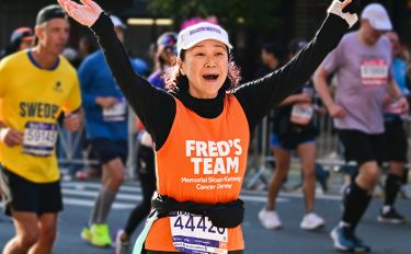 Runner joyfully raises arms during a marathon, wearing an orange race bib.