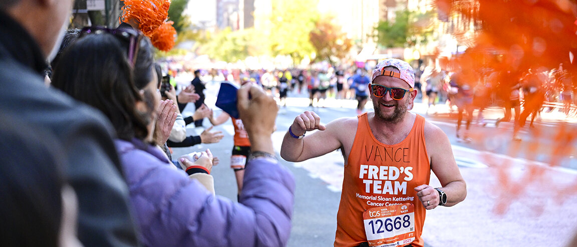 A runner in a tank top with his name, Vance, written above “Fred’s Team,” gestures to a cheering crowd during the TCS New York City Marathon. 