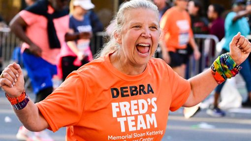 A Fred's Team charity runner wearing an orange uniform participating in the TCS New York City Marathon to raise money for cancer research.