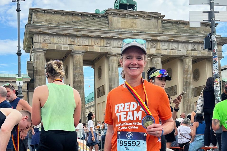 Fred’s Team charity runner Nicole standing in front of the Brandenburg Gate smiling and holding her finisher’s medal from the 2025 BMW Berlin Marathon.