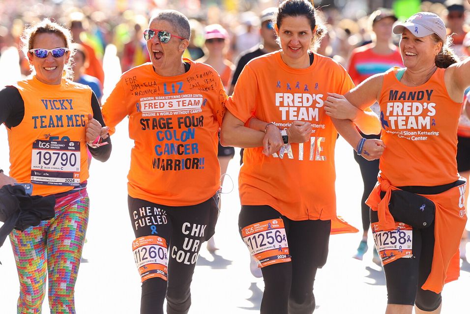Liz Healy and three of her Fred’s Team teammates on the TCS New York City Marathon course with their arms interlocked.