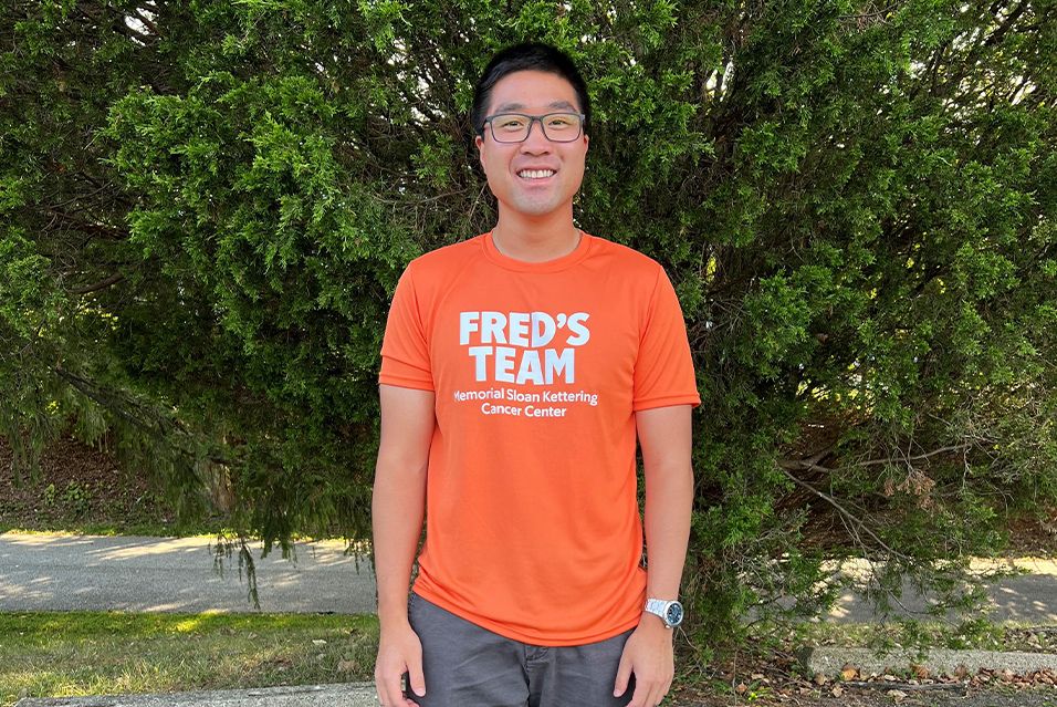 A Fred’s Team participant standing outdoors in front of green bushes, smiling at the camera. 