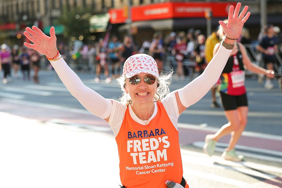 A participant wearing a Fred’s Team tank top raises their arms in celebration while running the TCS New York City Marathon. 