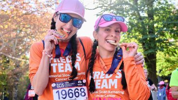 Two Fred’s Team runners biting their medals at the finish line of the 2024 TCS New York City Marathon.  