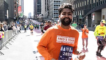 A person running while smiling and wearing an orange Fred’s Team shirt.